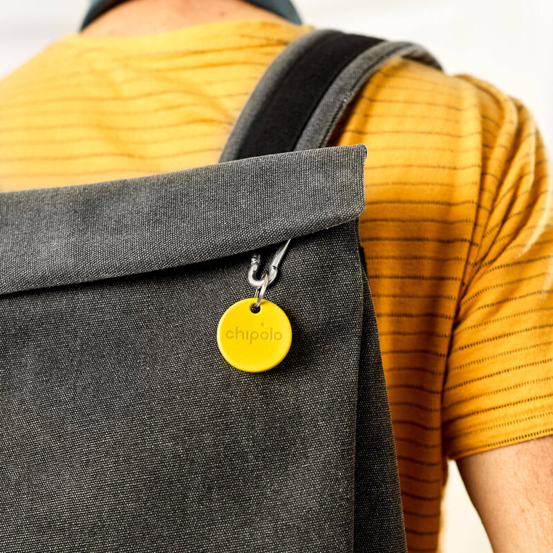 Ein gelber Chipolo Bluetooth-Tracker ist an einem grauen Rucksack befestigt, getragen von einer Person mit gelbem gestreiften T-Shirt.